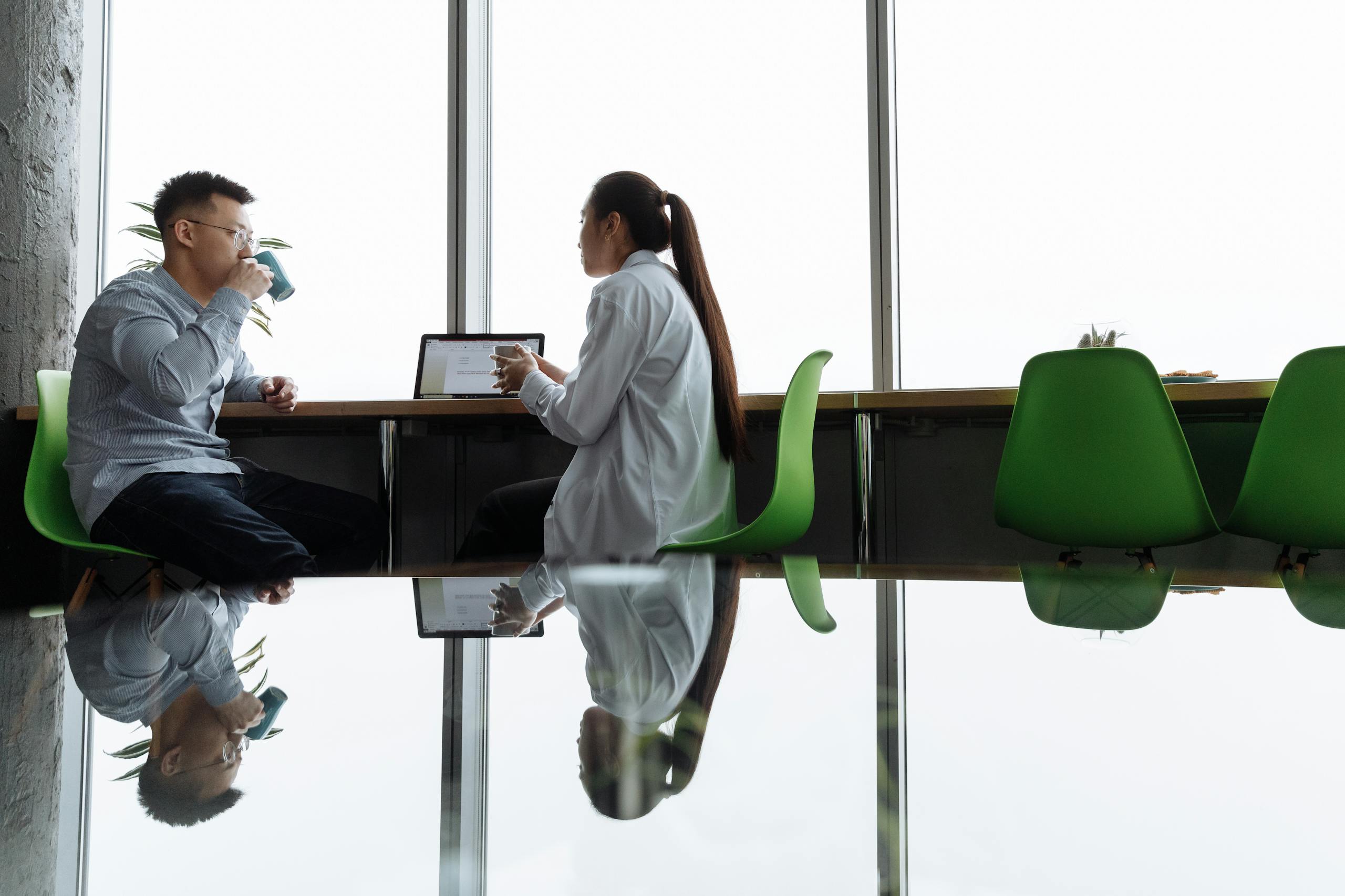 Two professionals discuss ideas in a modern office setting with vibrant green chairs.